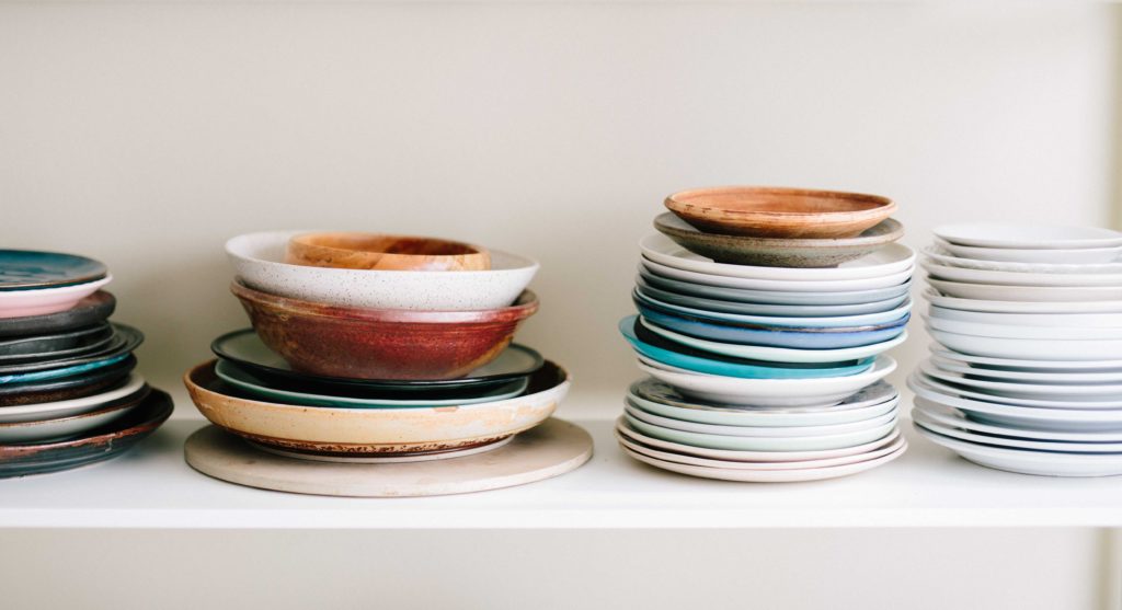 Dishes neatly piled up on dorm shelf.