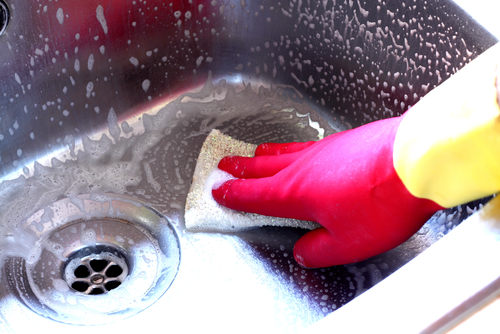 A person scrubs their kitchen sink with a scouring pad and gentle clenser.